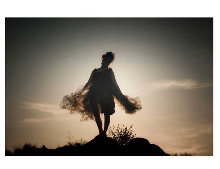 A silhouette of a woman standing on top of a hill