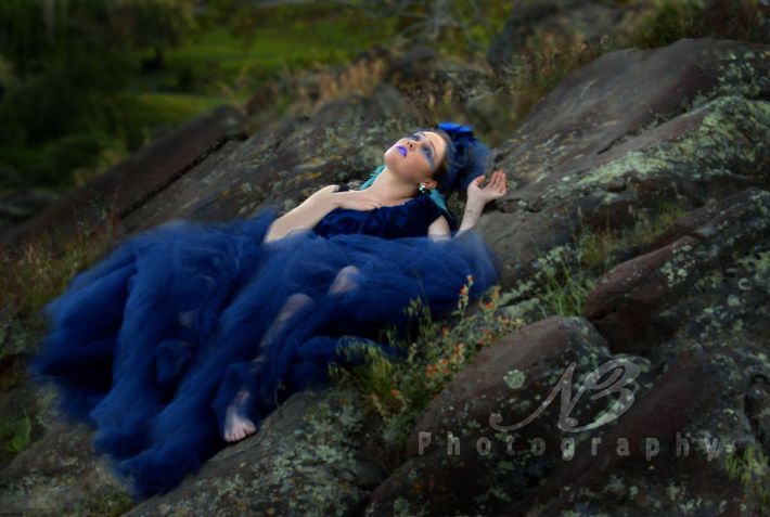 A woman in a blue dress is laying on a rock.