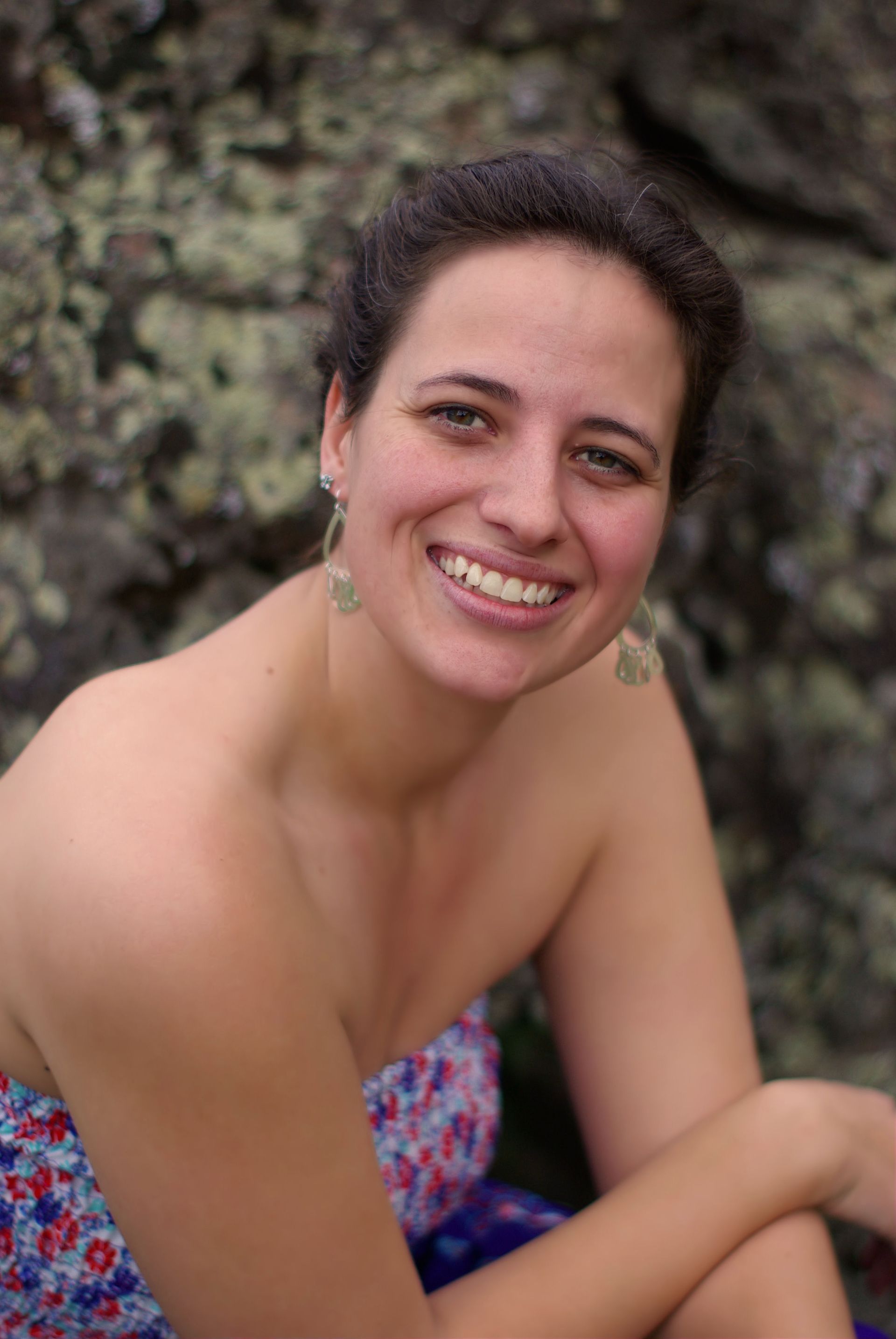 A woman is smiling while sitting on a rock.