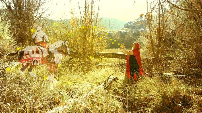 A woman in a red cape is standing in the middle of a field.