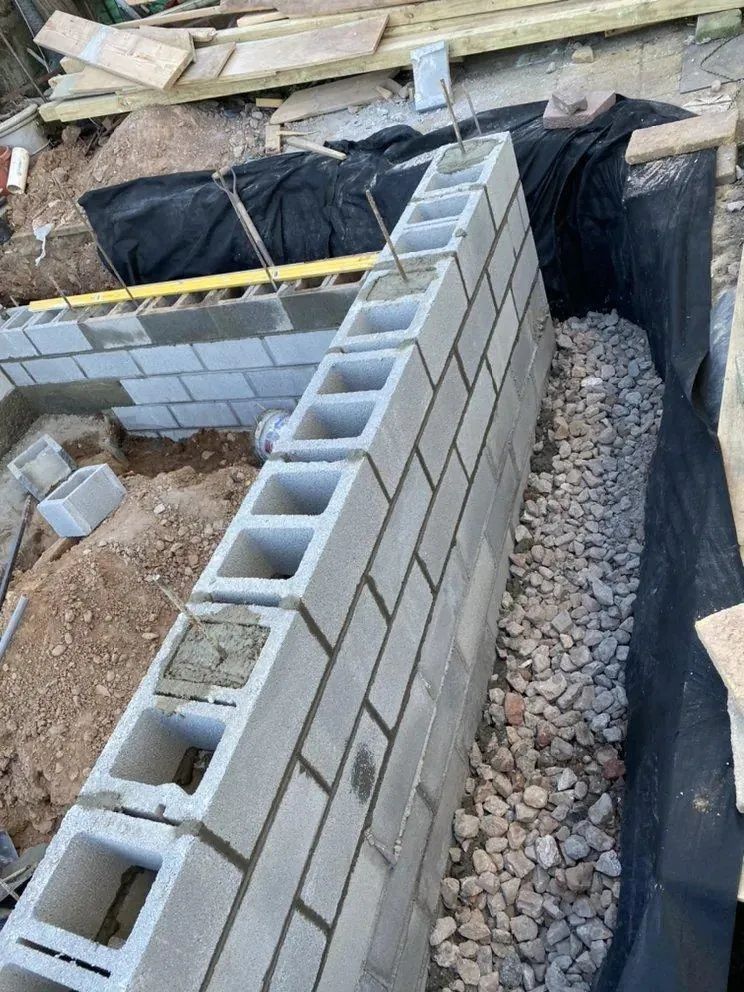 Construction site trench with cinder block wall, black plastic lining, and gravel base