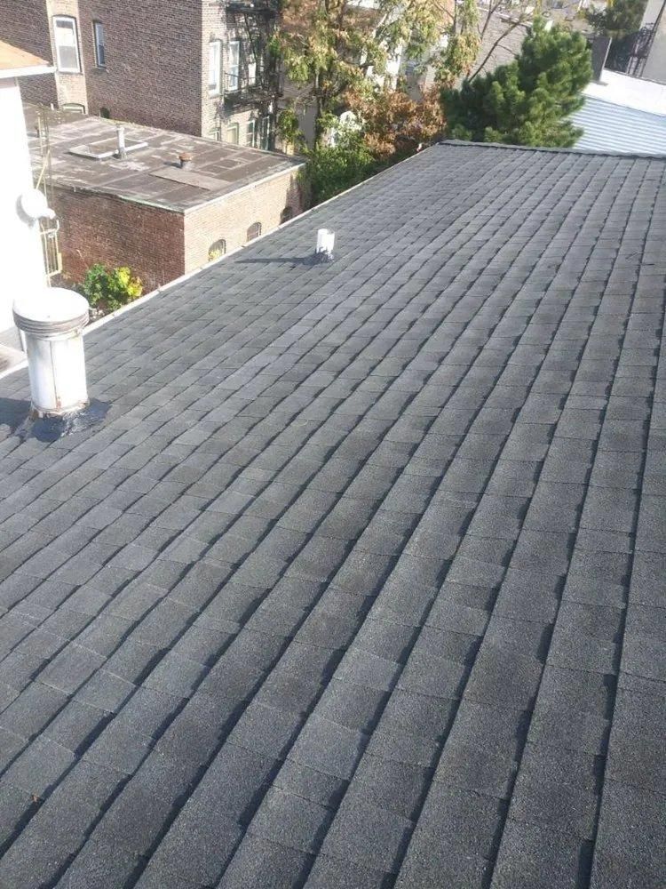 Dark gray shingled roof with a small white vent and neighboring brick houses in the background