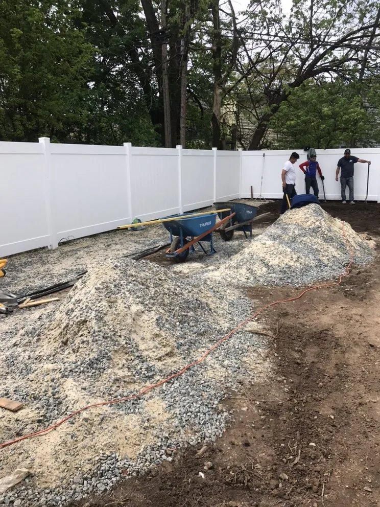 Workers moving gravel beside a white fence in a backyard construction area