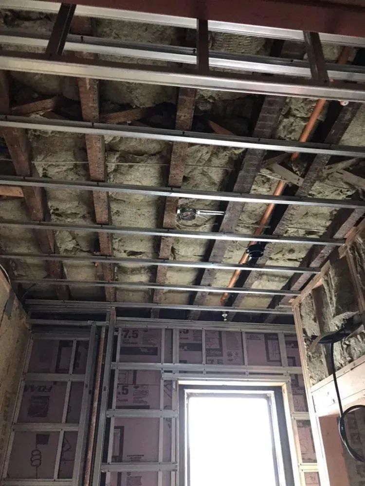 Exposed ceiling with metal framing and insulation above a room, with a bright window below
