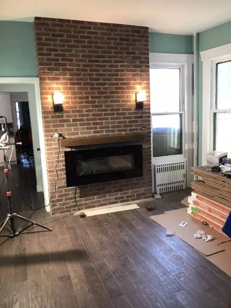 Living room with brick fireplace, dark wood floor, and renovation materials stacked by the wall