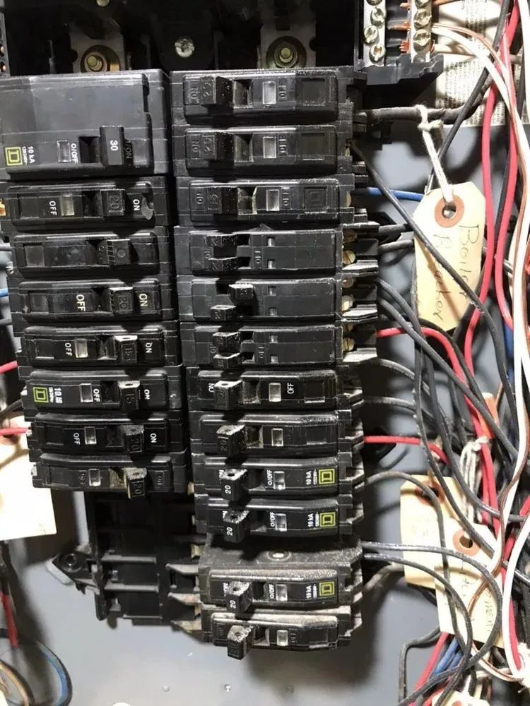 Close-up of an electrical breaker panel with rows of black circuit breakers and tangled wires inside