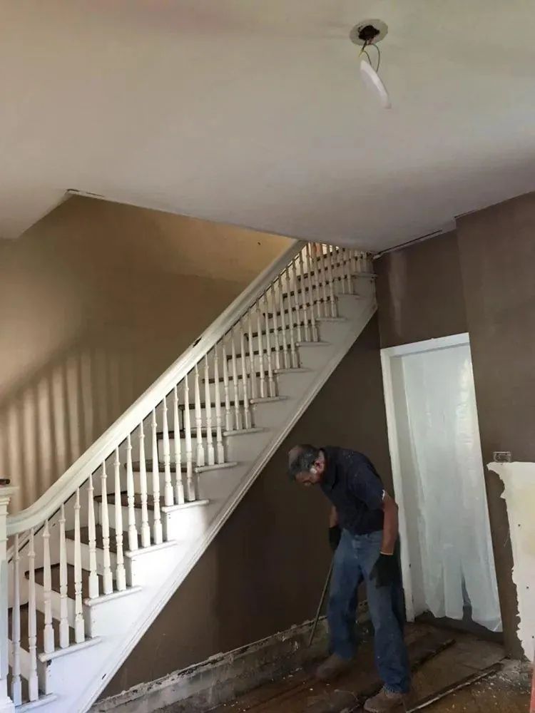Man standing under a staircase in an unfinished room with exposed walls and a hanging ceiling light