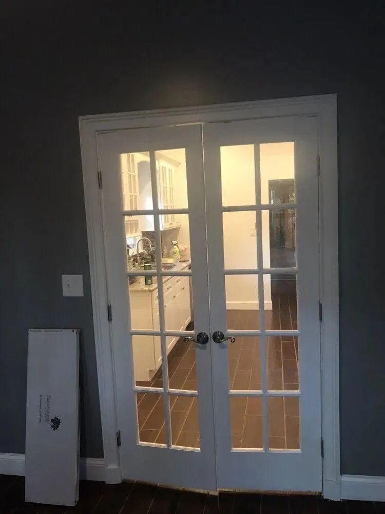 White French doors in a dark room, opening to a lit interior hallway with wood floors.