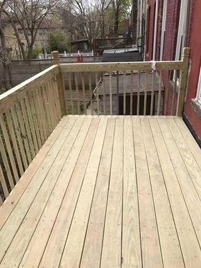 Wooden deck with railing beside a red building, overlooking a backyard.