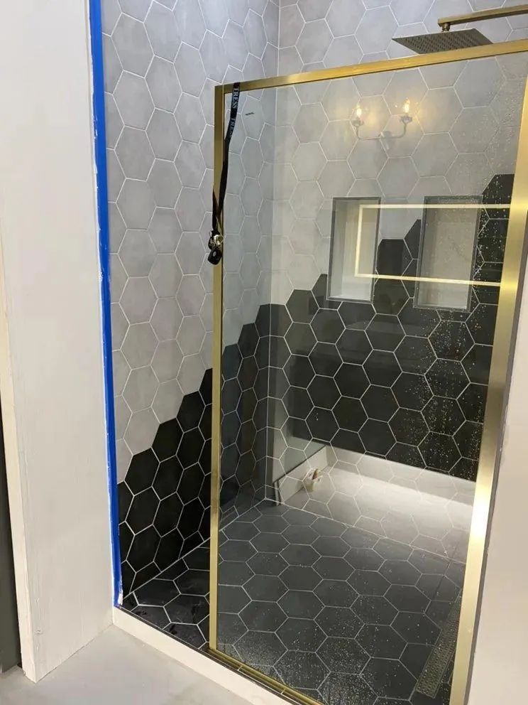 Mirror in a stairwell reflects a black hexagon-tiled wall and a doorway framed with gold trim.