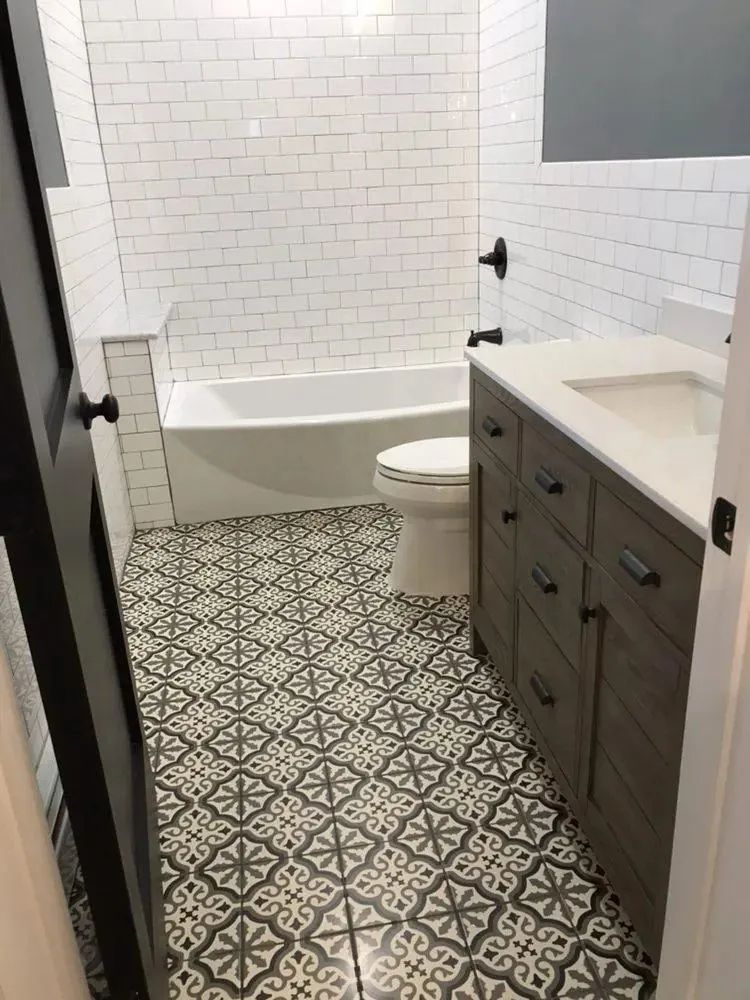 Small bathroom with a white tub, toilet, dark vanity, and patterned black-and-white tile floor.