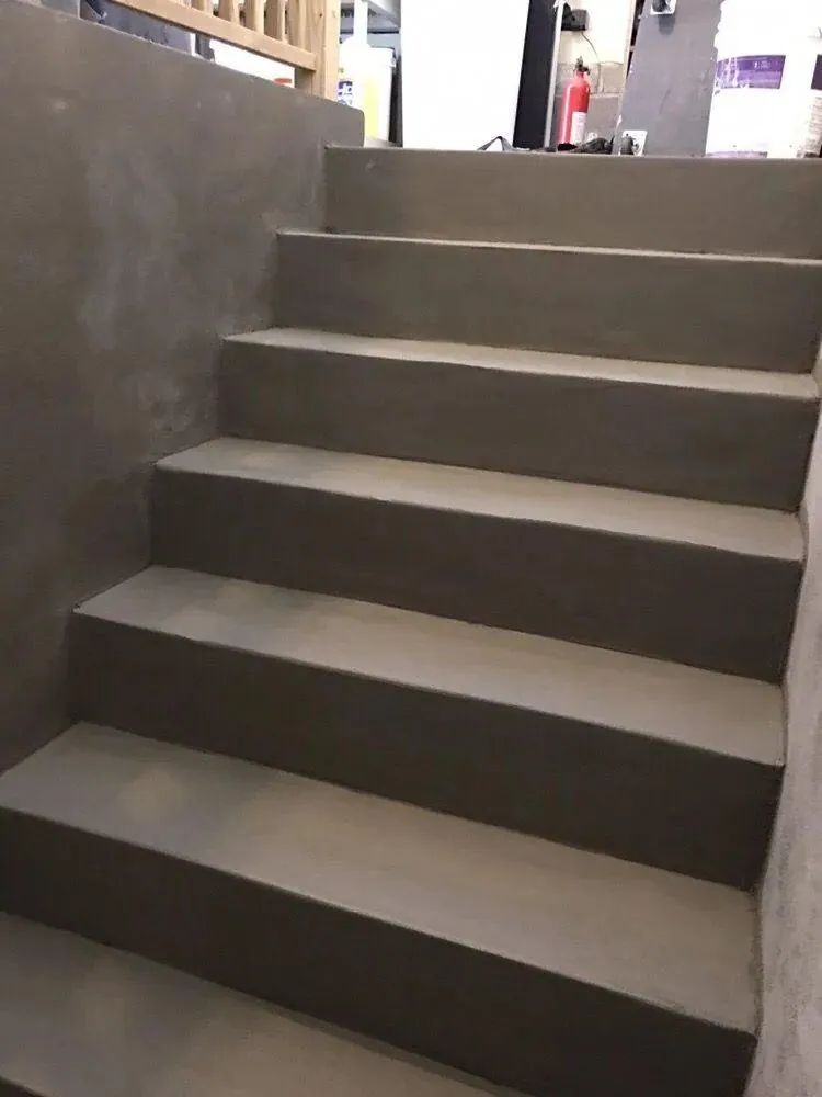 Gray concrete staircase indoors with five steps and a metal railing on the left