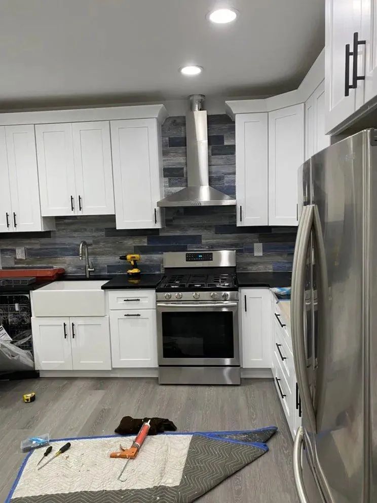Modern kitchen with white cabinets, stainless steel appliances, and tools on the floor during a renovation