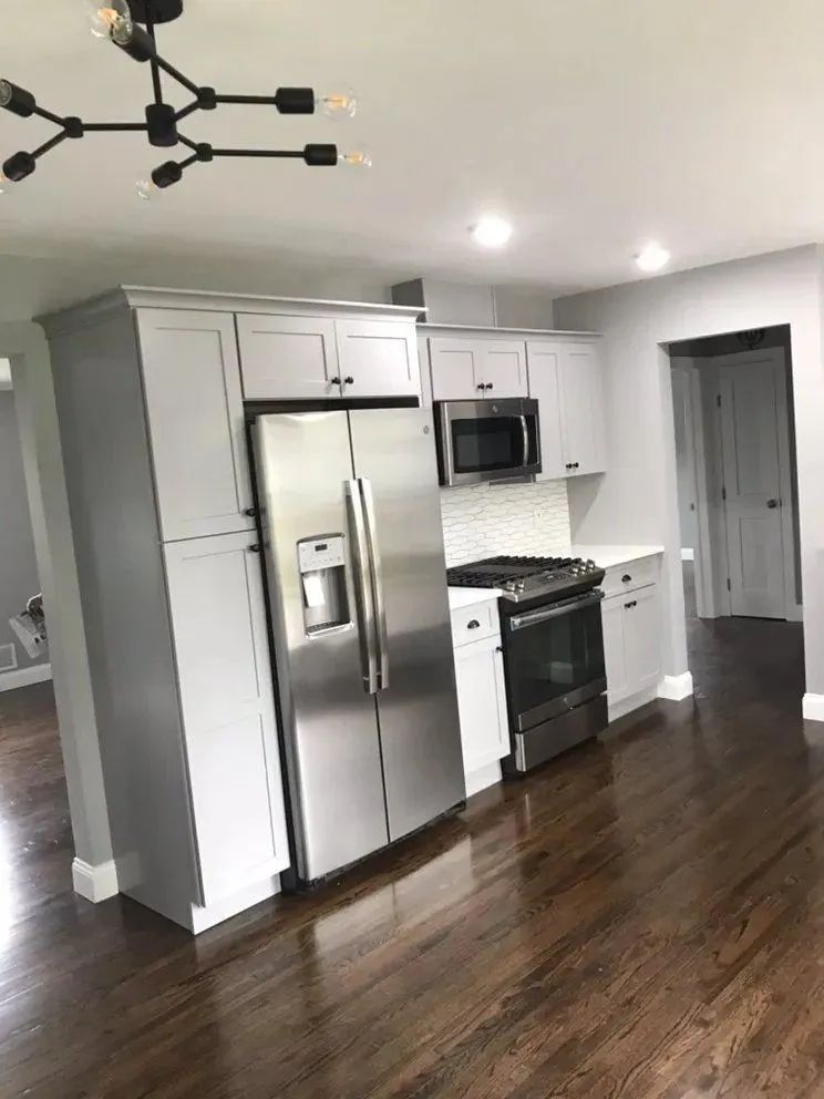 Empty modern kitchen with stainless steel appliances, white cabinets, and dark hardwood floors.