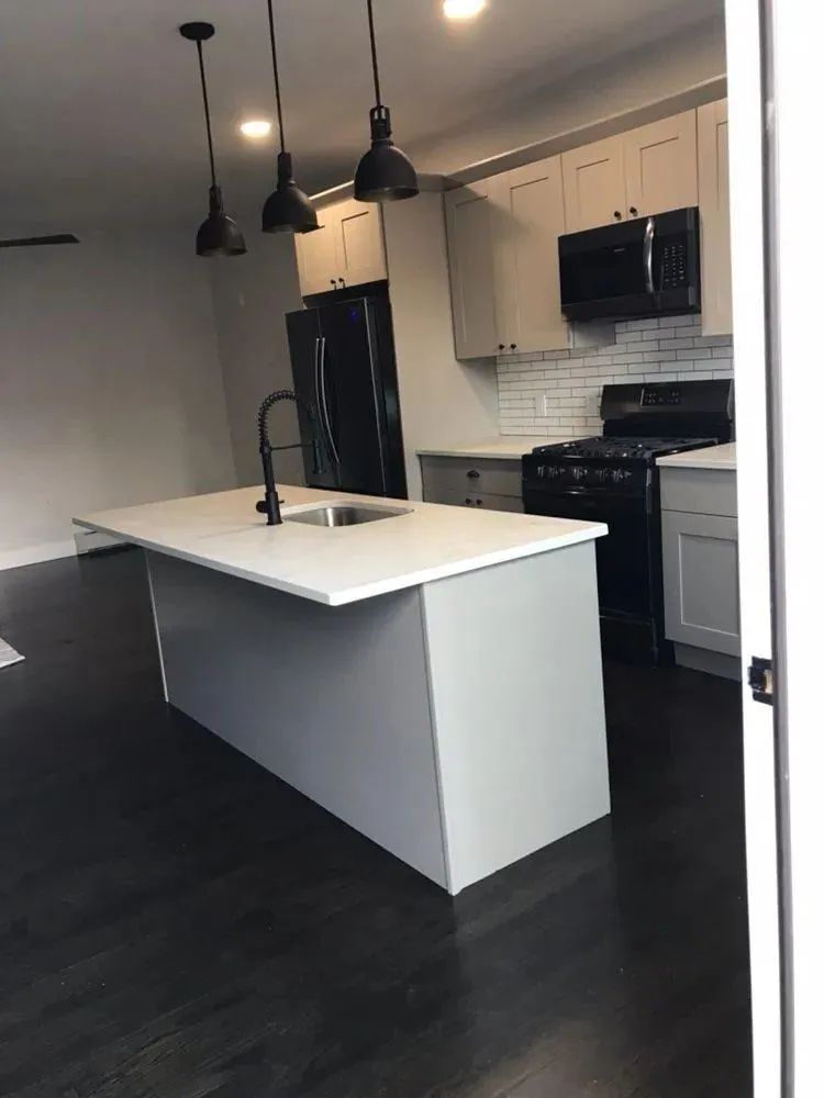 Modern kitchen with white island, black pendant lights, dark floor, and stainless steel appliances