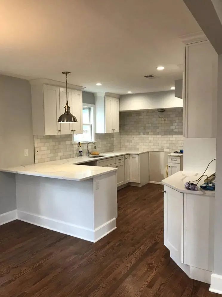 Modern white kitchen with island, pendant light, gray tile backsplash, and dark wood floors