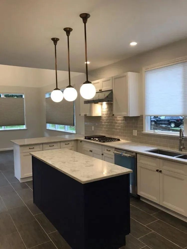 Modern kitchen with dark tile floor, white cabinets, marble island, and hanging pendant lights