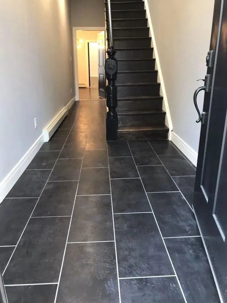 Narrow hallway with dark tile floor leading to a staircase at the far end.