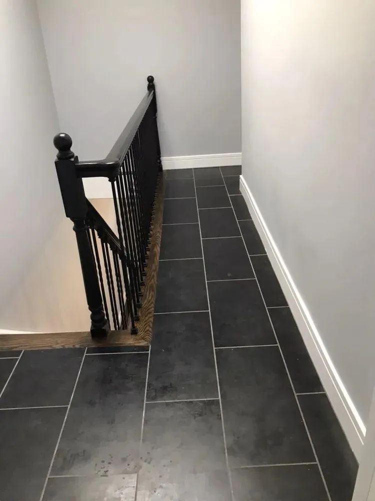 Narrow hallway with black tiled floor and a black stair railing along the left side