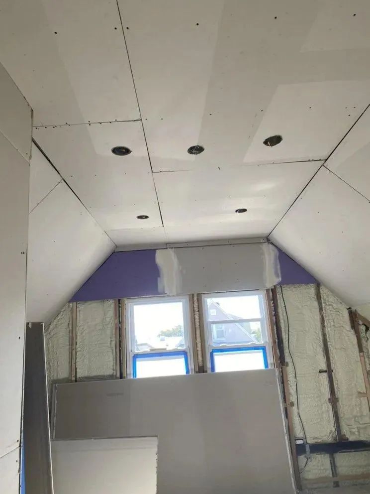Unfinished attic room with sloped white ceiling, skylight windows, and drywall panels in progress
