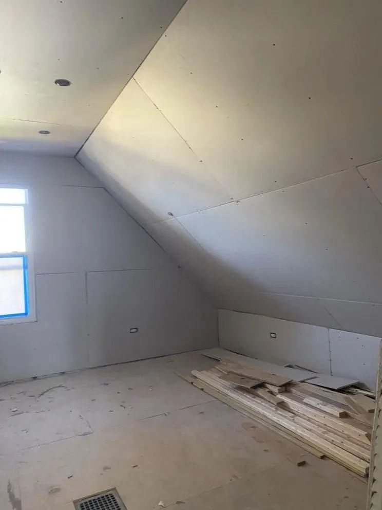 Unfinished attic room with sloped ceiling, window, and construction materials on the floor