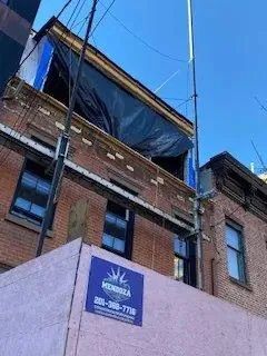 Brick building with a blue tarp-covered roof and a construction sign against a clear blue sky
