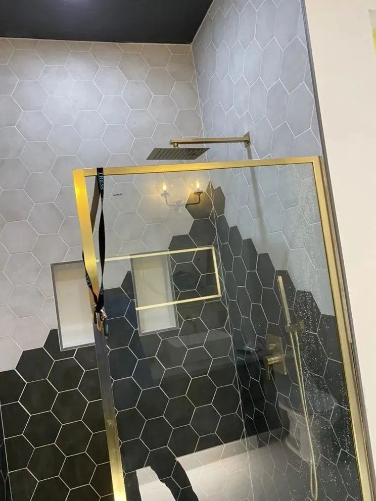 Gold-framed glass staircase with black and white tiled walls and floor in a modern interior