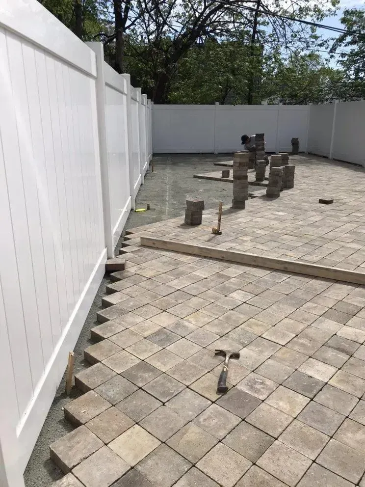 Empty patio with paver flooring, white fence, and several utility posts in a fenced yard