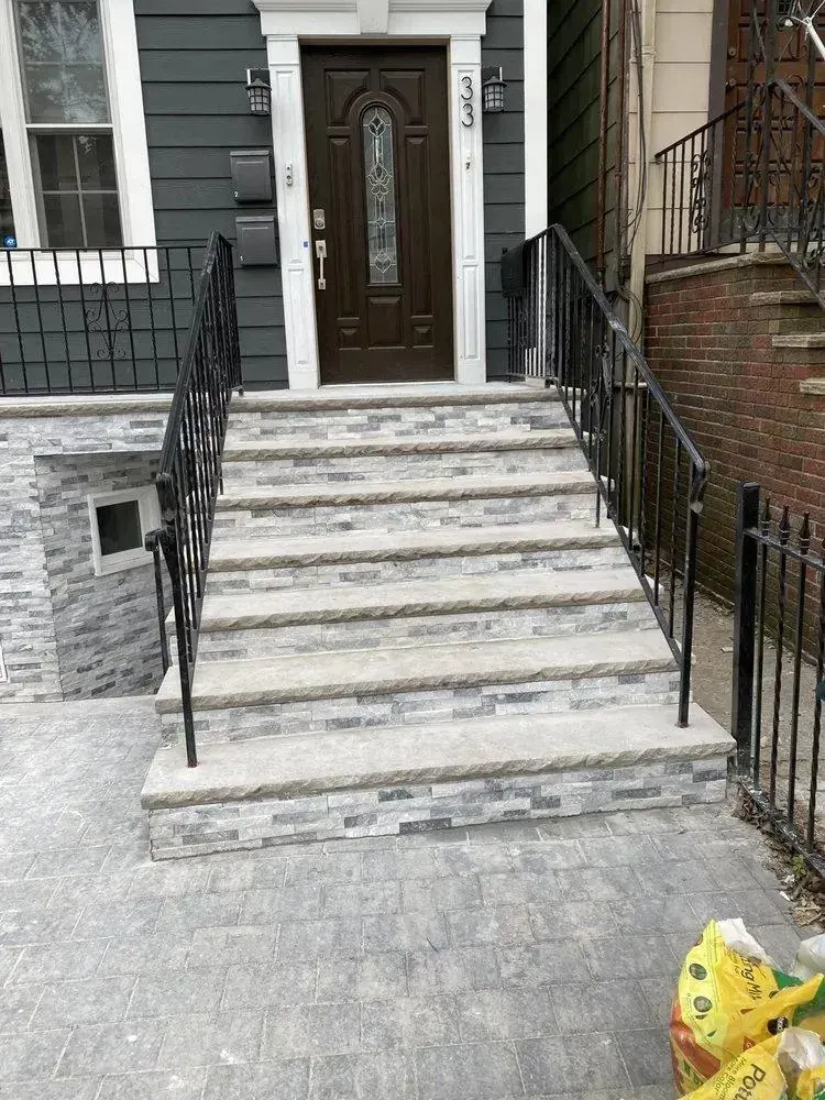 Front entrance with marble steps, black railings, and a dark wooden door on a brick townhouse.