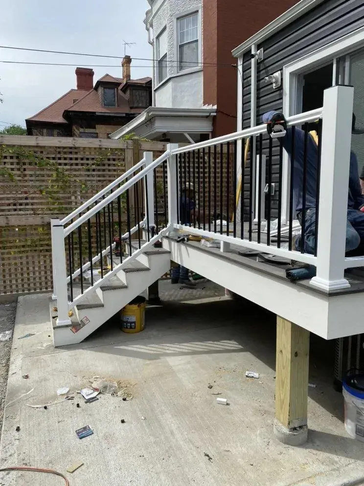 Outdoor front porch with white stairs and railing beside a black house, showing a concrete driveway below.