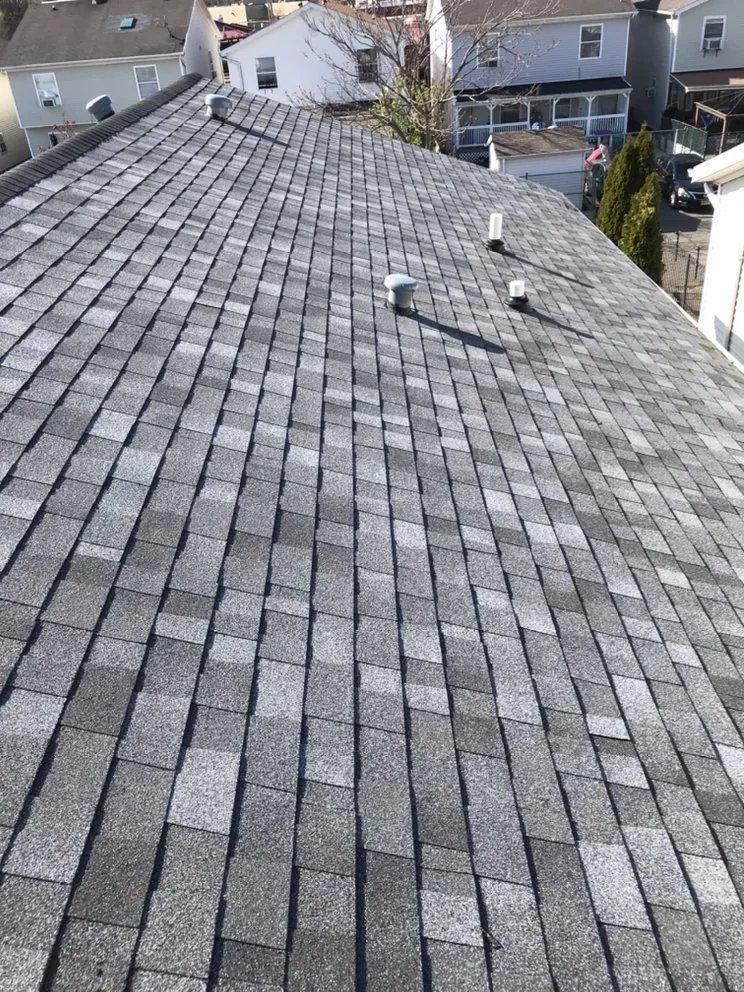 Gray shingled rooftop with vents and neighboring houses in the background