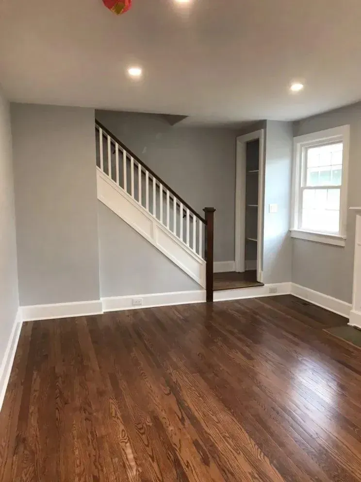 Empty living room with dark wood floors, gray walls, and a staircase in the back.