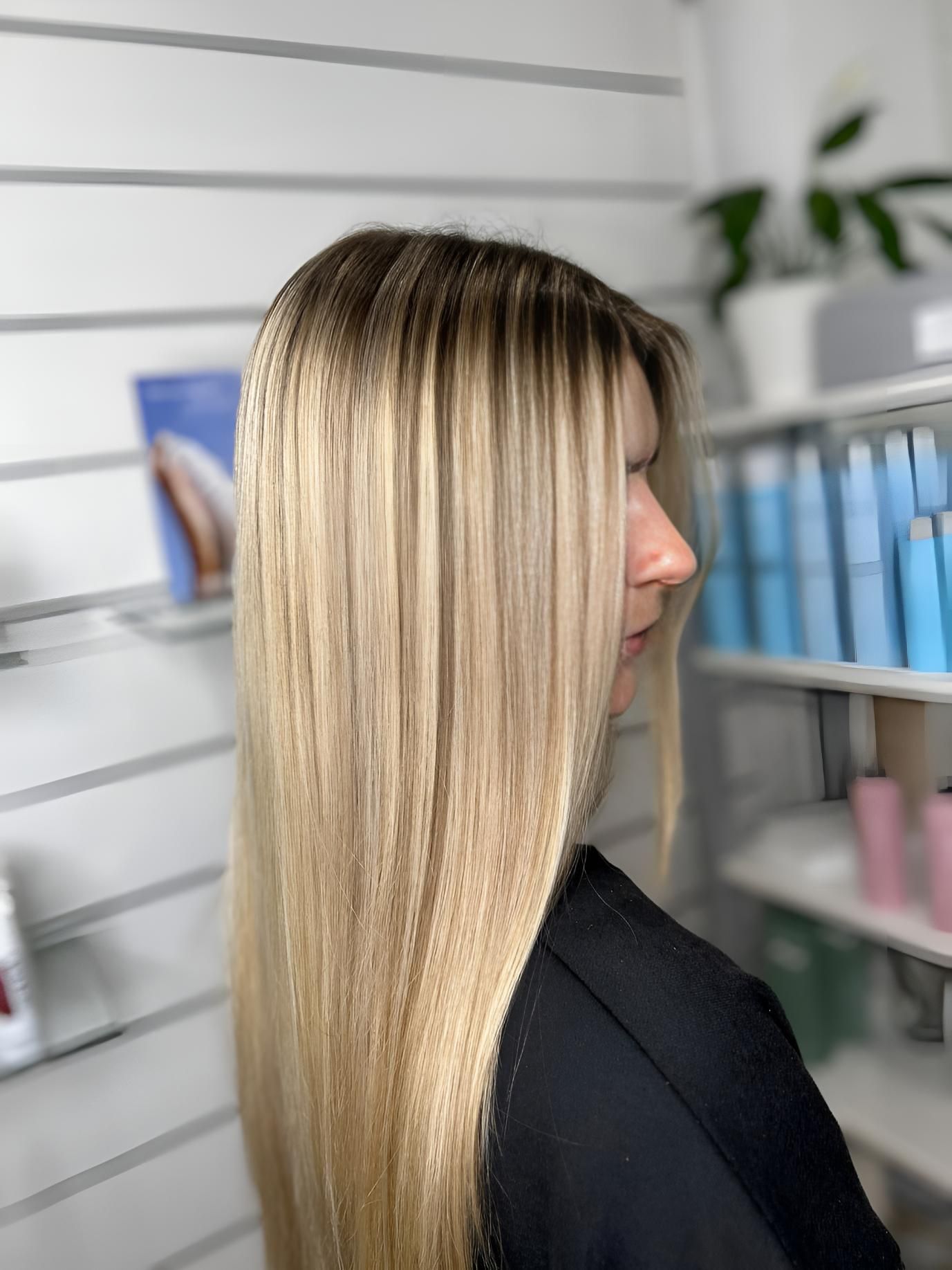 A Woman With Long Blonde Hair is Standing in Front of a Shelf of Hair Products — Strut Hair & Beauty In Maroochydore, QLD