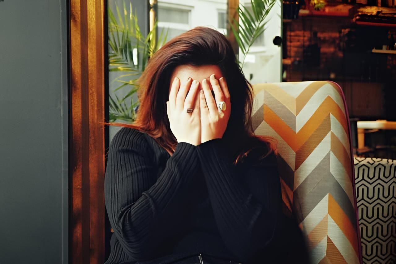 A Woman is Covering Her Face With Her Hands While Sitting in a Chair — Strut Hair & Beauty In Maroochydore, QLD