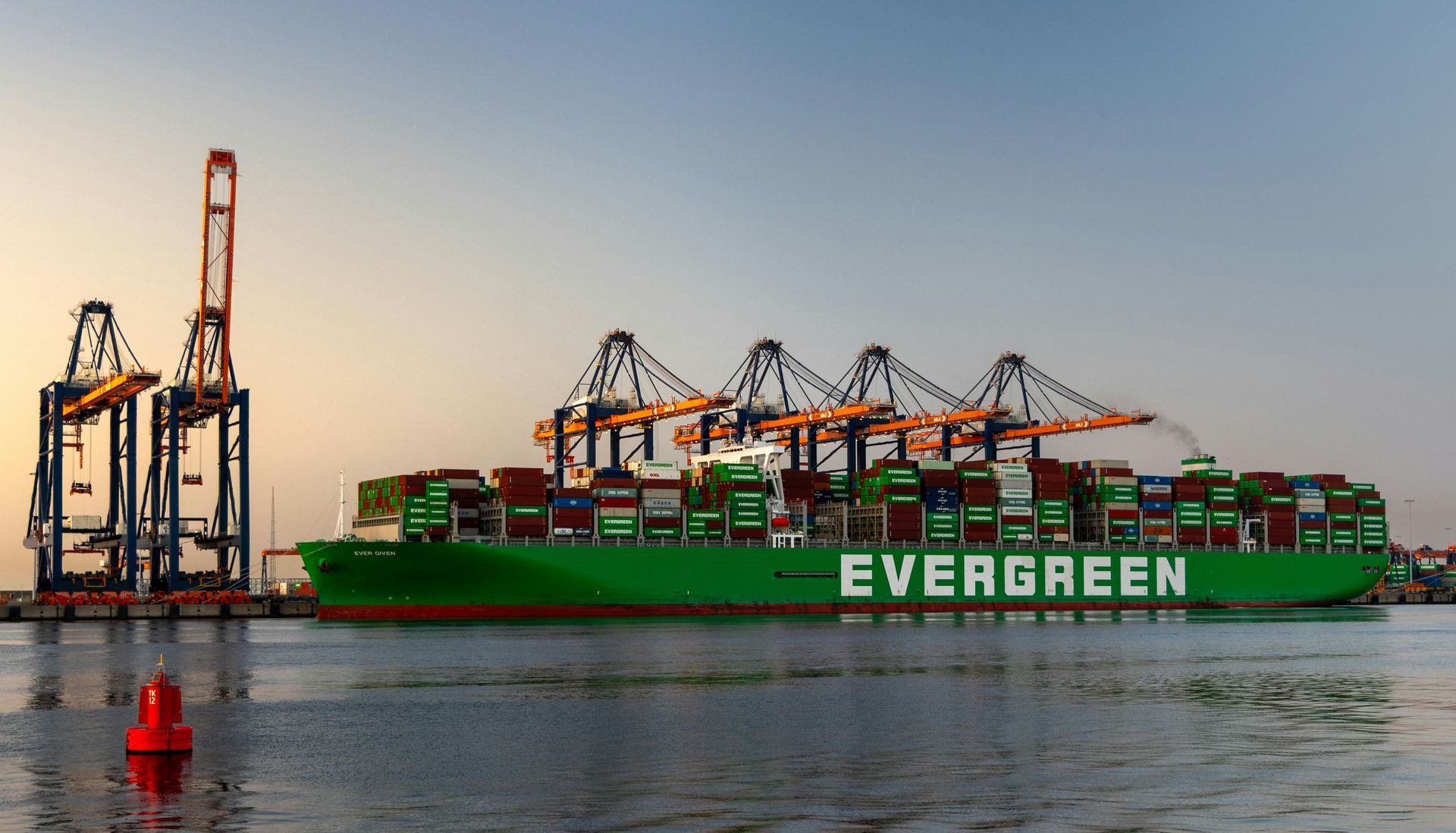 Um grande navio porta-contêineres verde e perene está atracado em um porto.