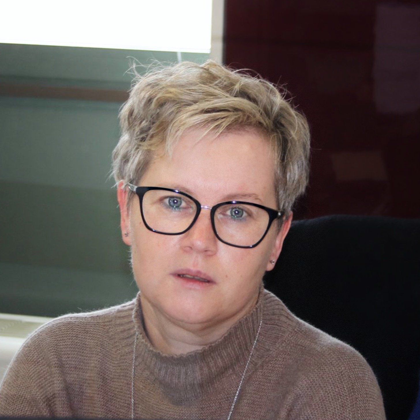 Una donna che indossa occhiali e un maglione marrone guarda la telecamera