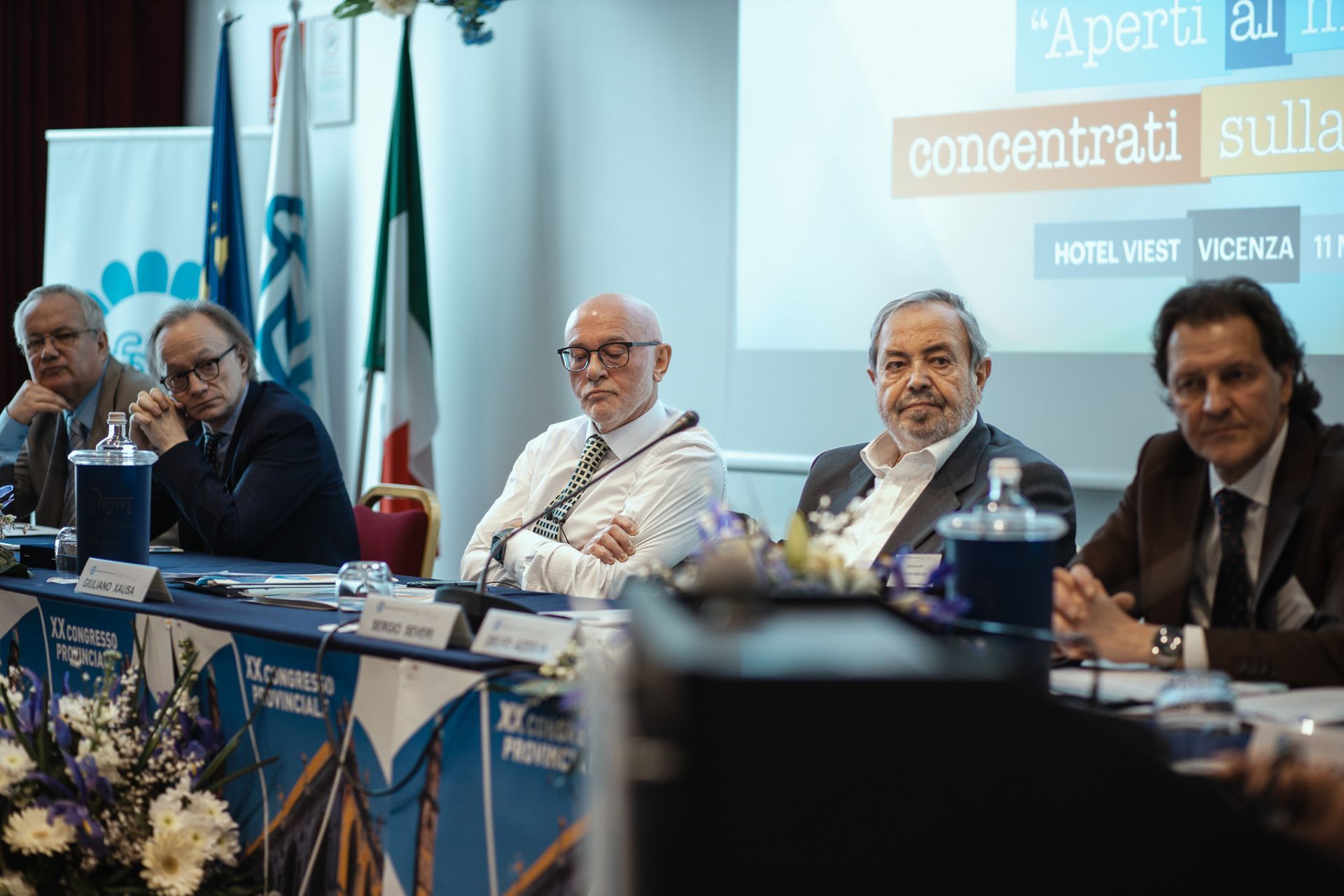 Un gruppo di uomini è seduto a un tavolo davanti allo schermo di un proiettore.