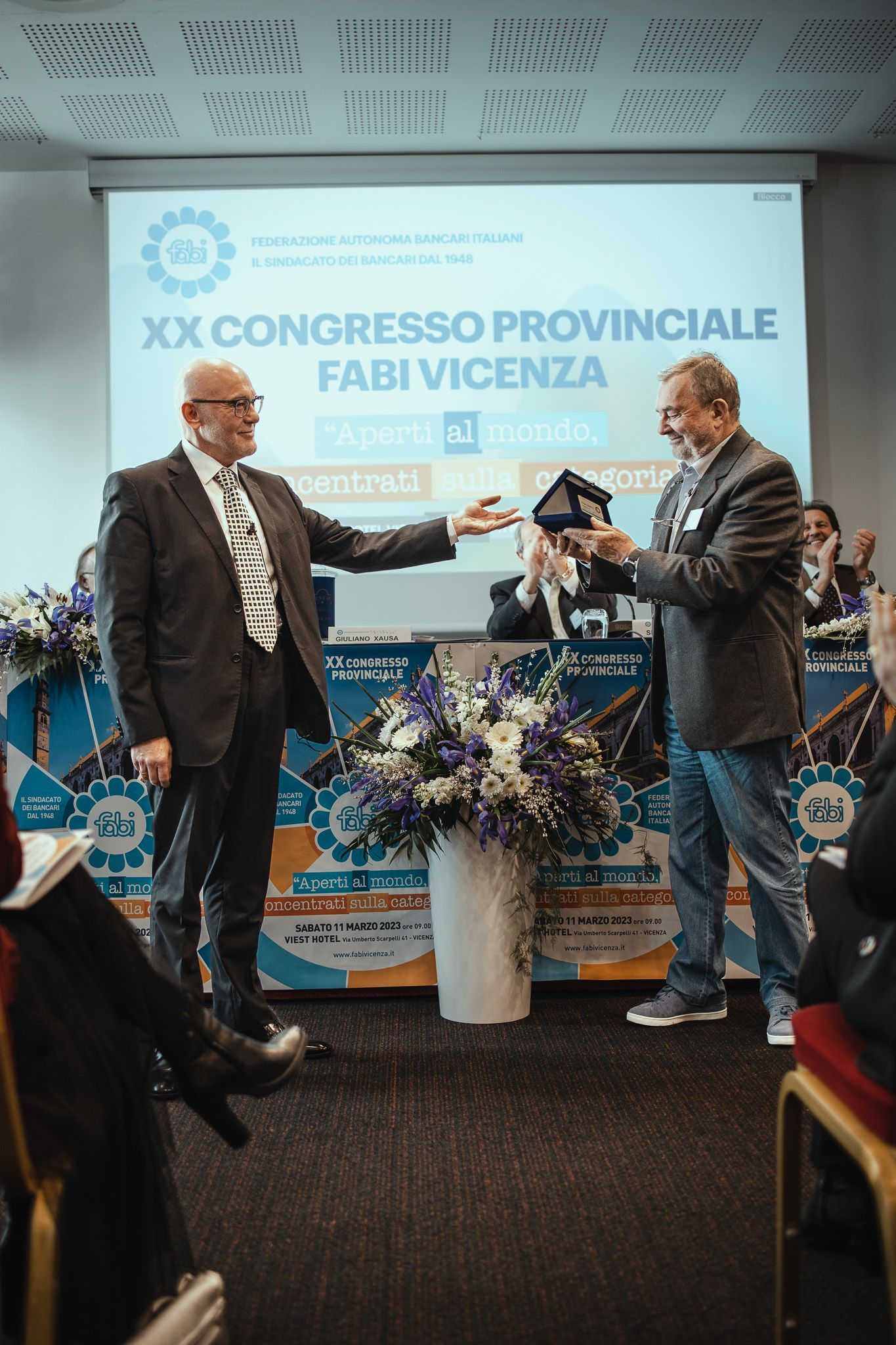 Due uomini sono in piedi davanti allo schermo di un proiettore durante una conferenza.