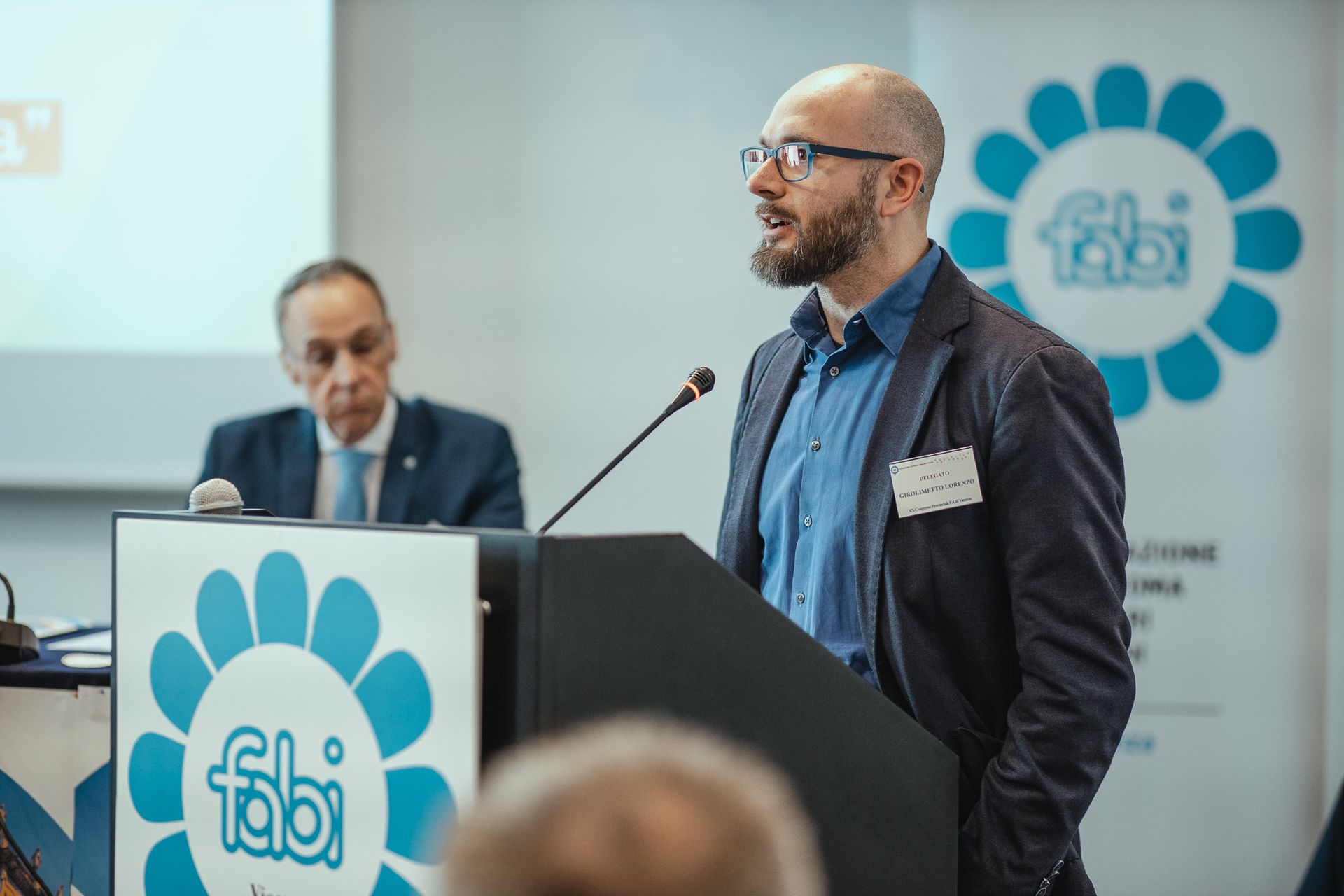 Un uomo è in piedi su un podio e fa una presentazione a un gruppo di persone.
