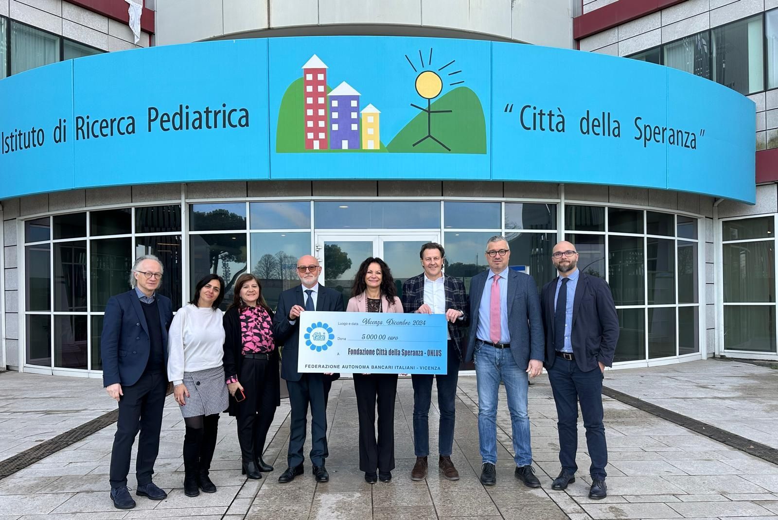 Un gruppo di persone è in piedi davanti a un edificio e tiene in mano un assegno di grandi dimensioni.