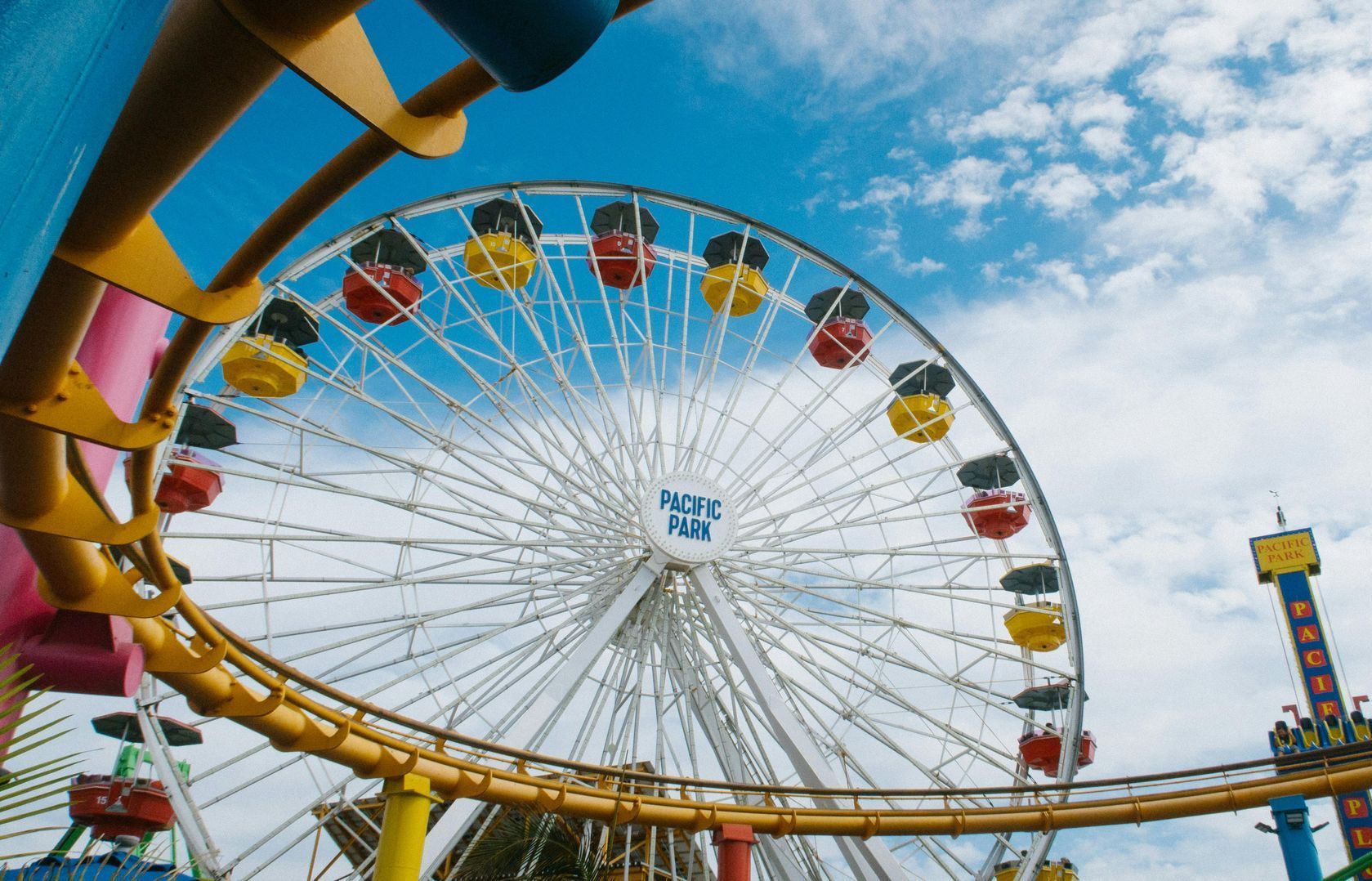 Una ruota panoramica in un parco divertimenti con delle montagne russe sullo sfondo.