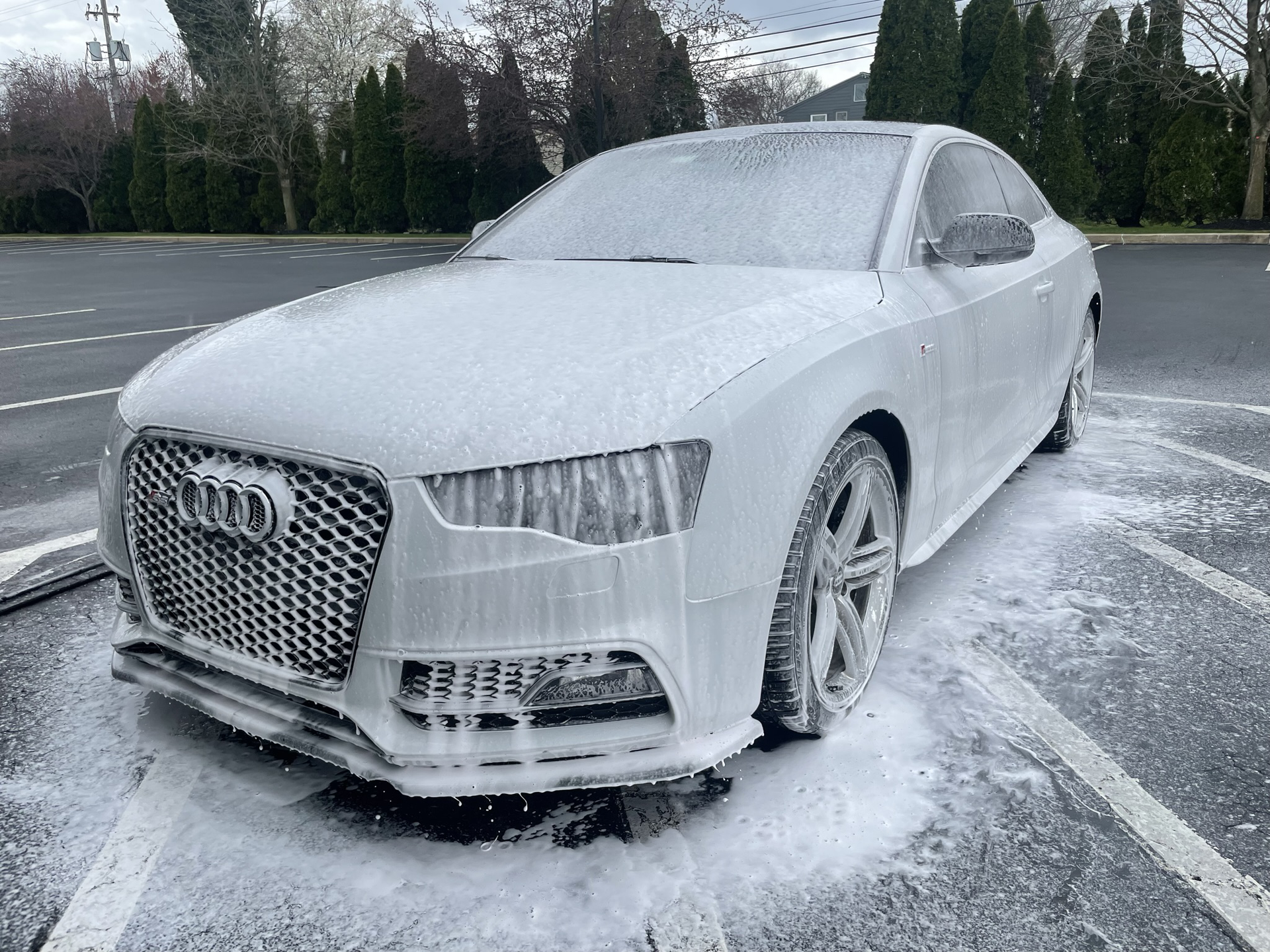 A white audi s5 is covered in foam in a parking lot.