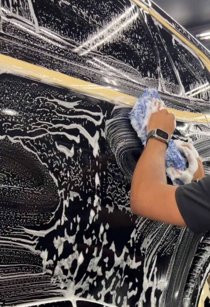 A person wearing black gloves is cleaning a black car with a blue cloth.