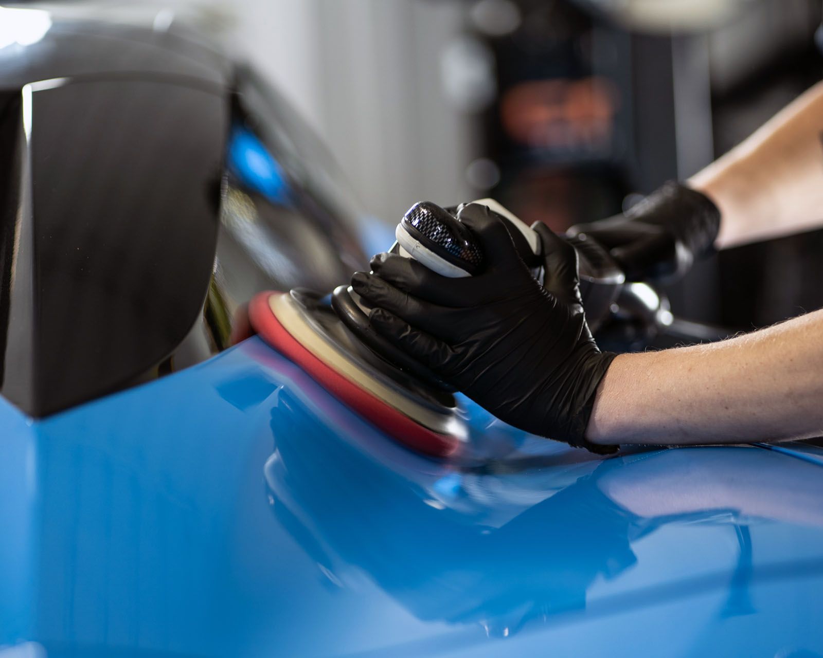 A person is polishing a blue car with a machine.
