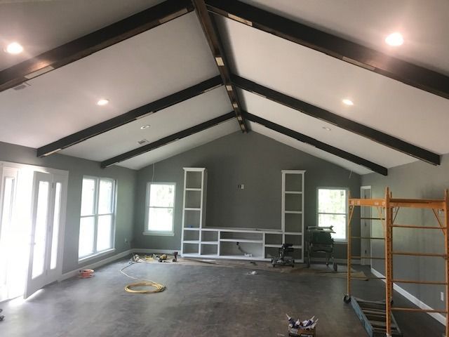 Interior of a vaulted room under renovation, with gray walls, exposed beams, windows, and scaffolding.