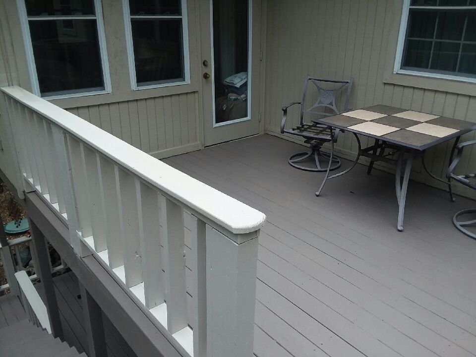 Wooden deck with beige siding, railing, sliding door, and patio table and chairs.