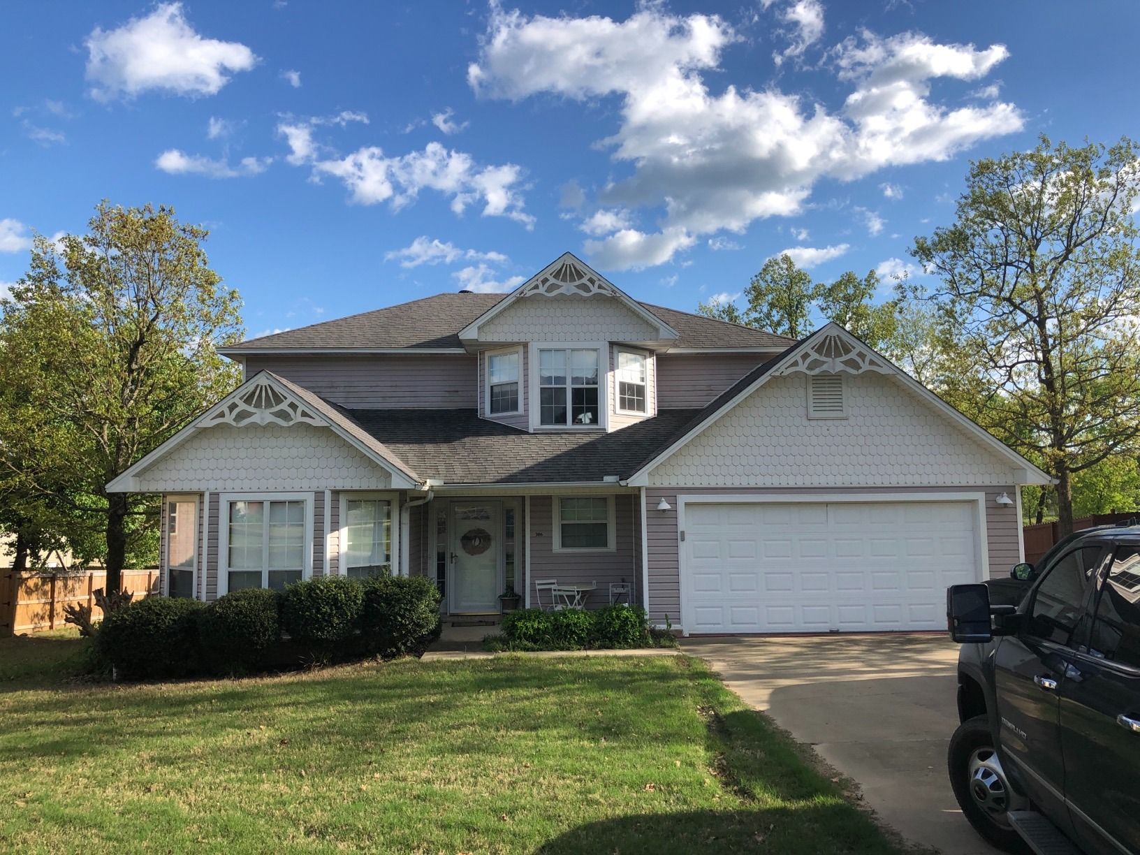 Suburban house with gray siding, front lawn, and a white garage under a partly cloudy sky
