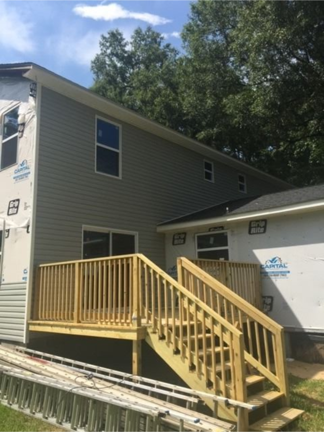Gray house with a yellow wooden ramp and stairs leading to a side entrance.