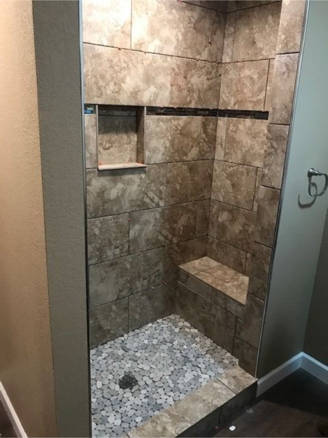 Walk-in stone shower with pebble floor, built-in shelf, and bench seat under a rainfall showerhead