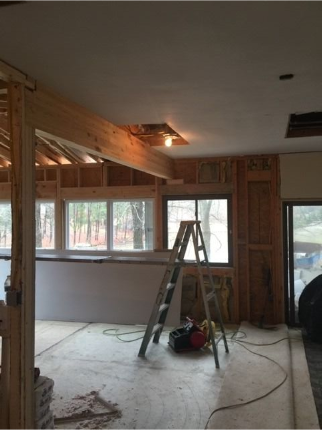 Partially renovated room with exposed beams, windows, and a ladder on the floor